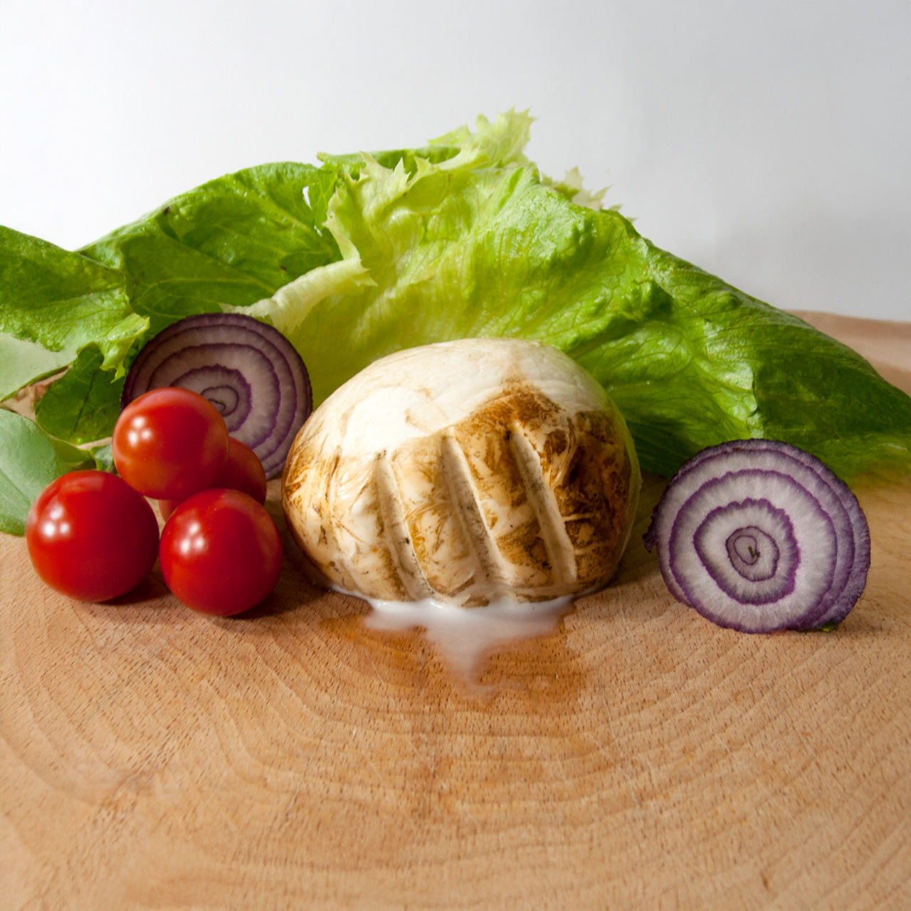 Provola affumicata di latte di bufala Casabufala appoggiata su un tagliere con pomodori, insalata e cipolla